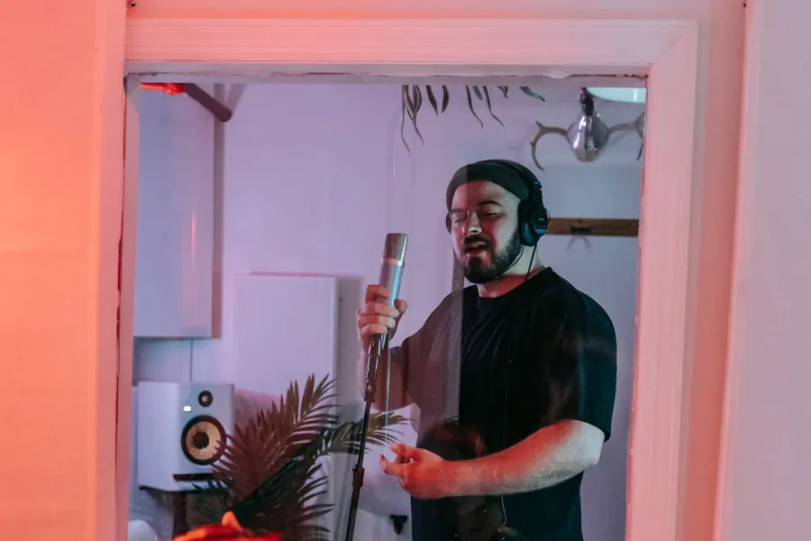 Vocal booth seen through a studio window with a singer in headphones