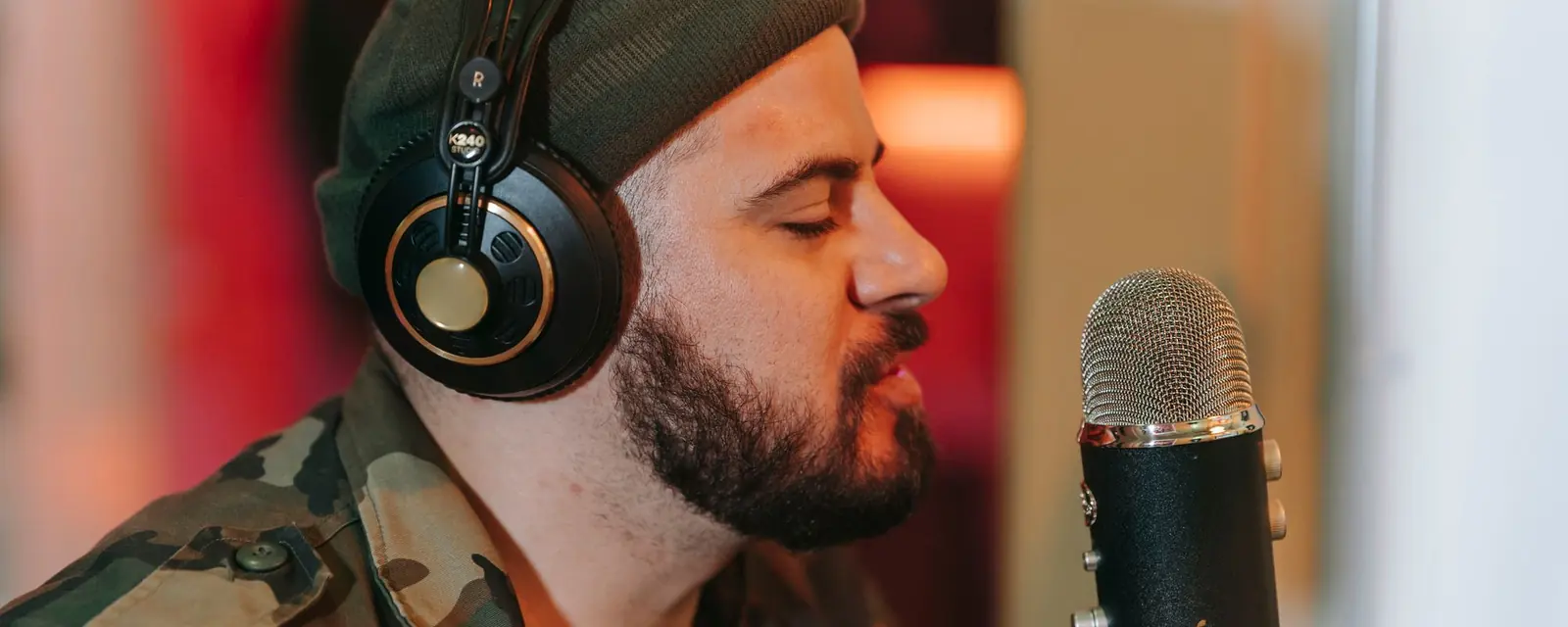 Singer wearing headphones recording vocals into a studio condenser microphone