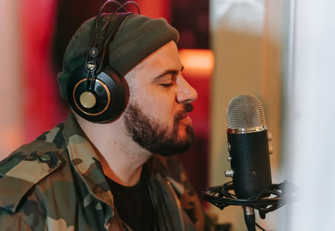 Singer wearing headphones recording vocals into a studio condenser microphone