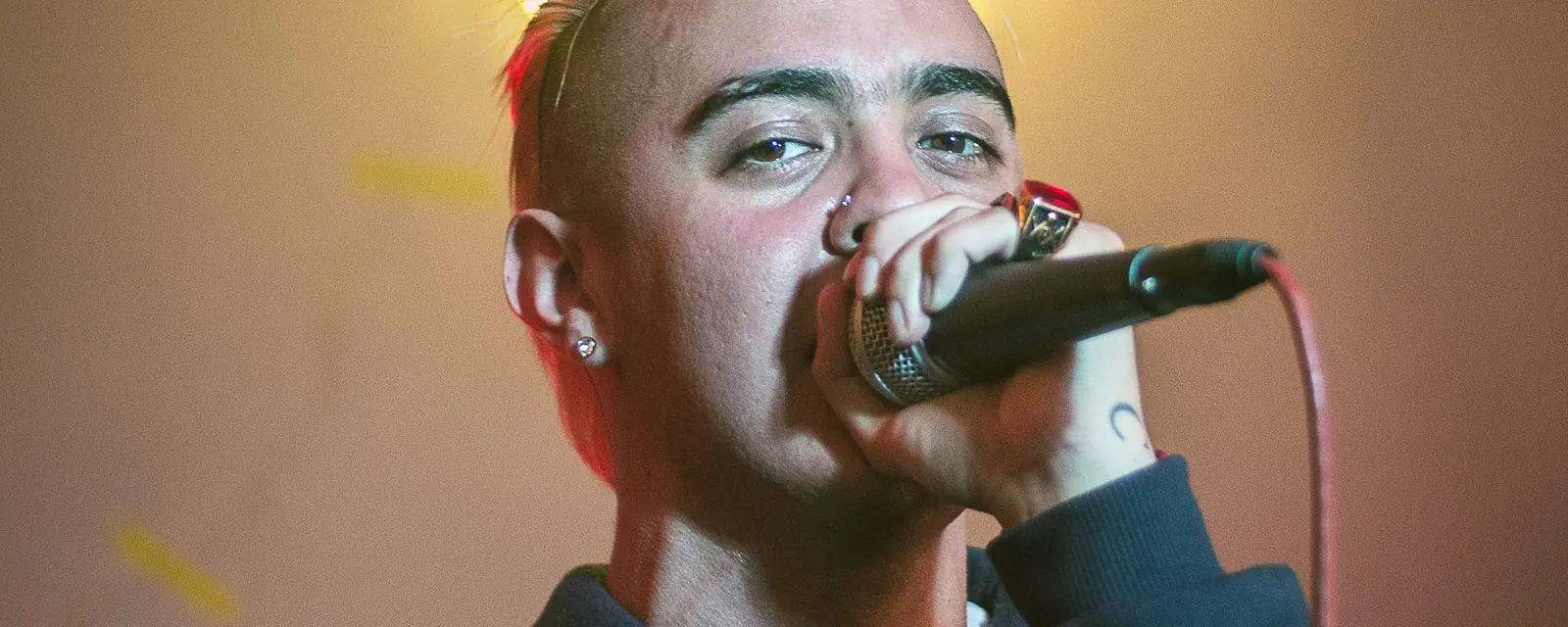 Rapper performing into a microphone in front of a neon sign