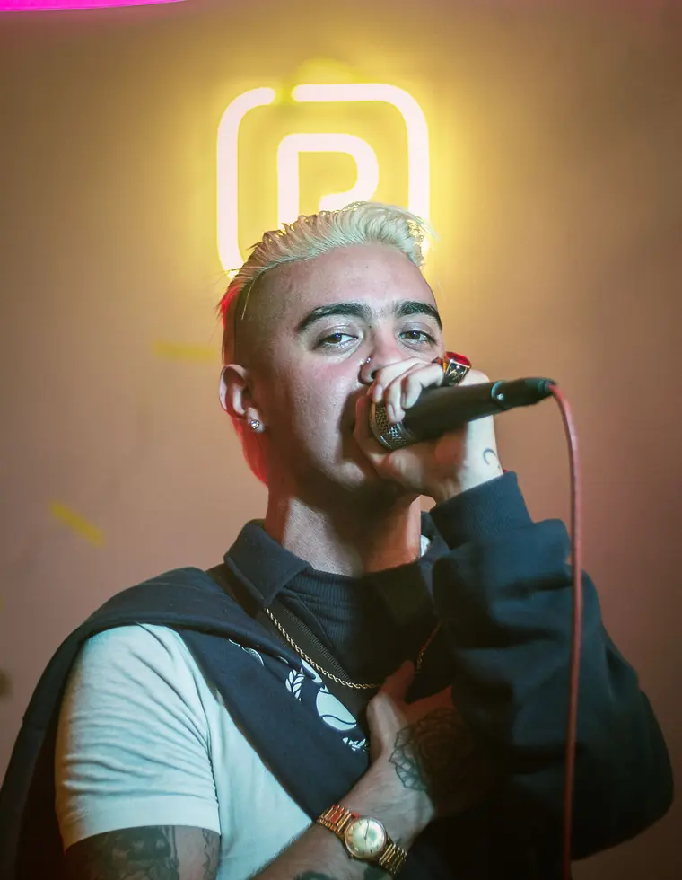 Rapper performing into a microphone in front of a neon sign